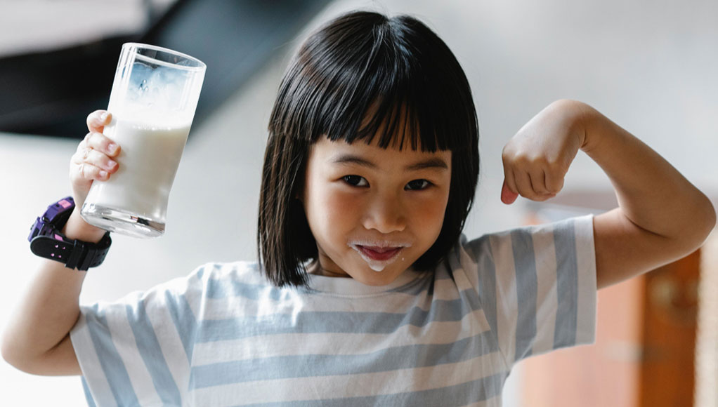 a young girl with a pint glass of milk in her hand with milk on her face