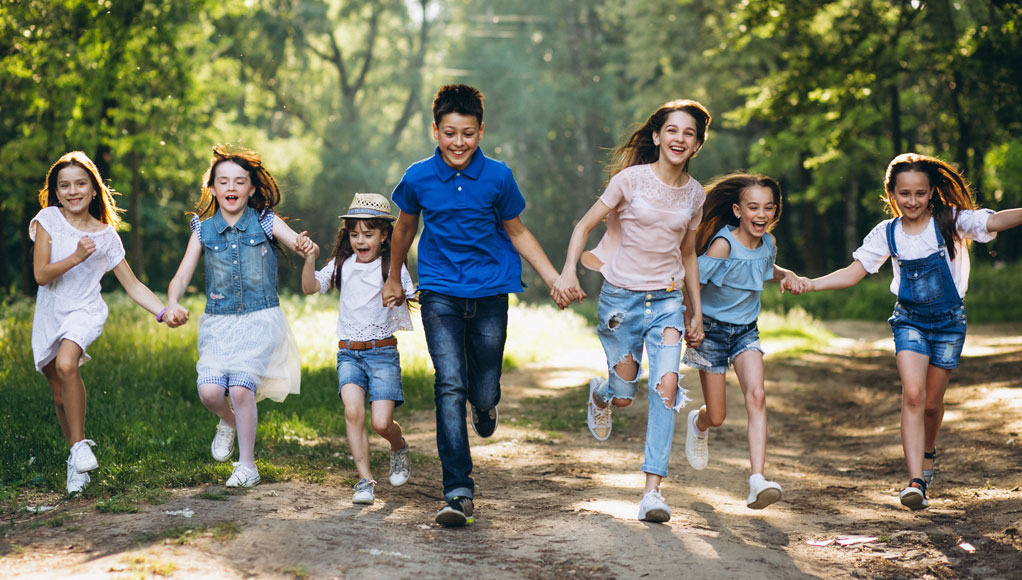 two teenagers and 3 small kids running happily on a forest road