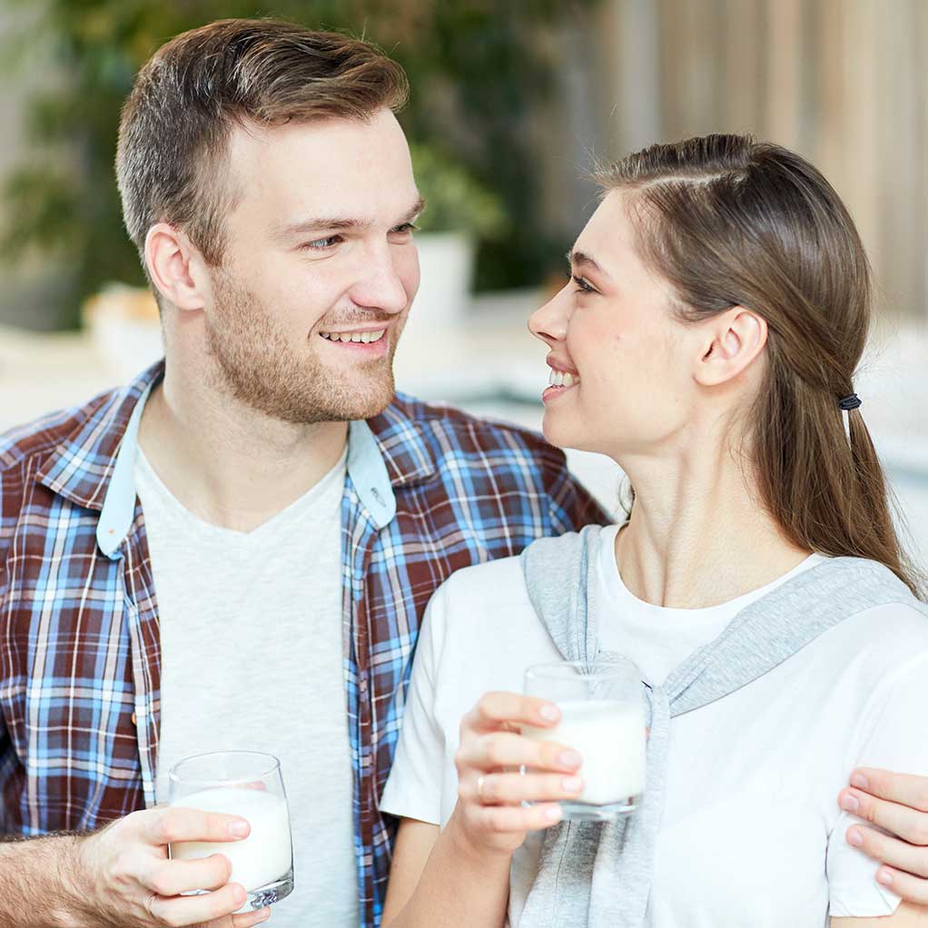 a young couple looking at each other happily drinking a glass a milk each